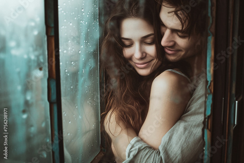 a young man hugging his girlfriend while both enjoy the closeness at a window covered with raindrops © L.S.