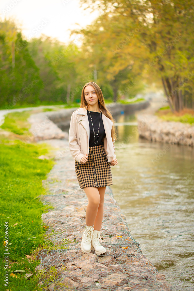 A young smiling girl walking in an autumn park in a good mood. Teenage girl, portrait against a background of nature. Fashion style trend.