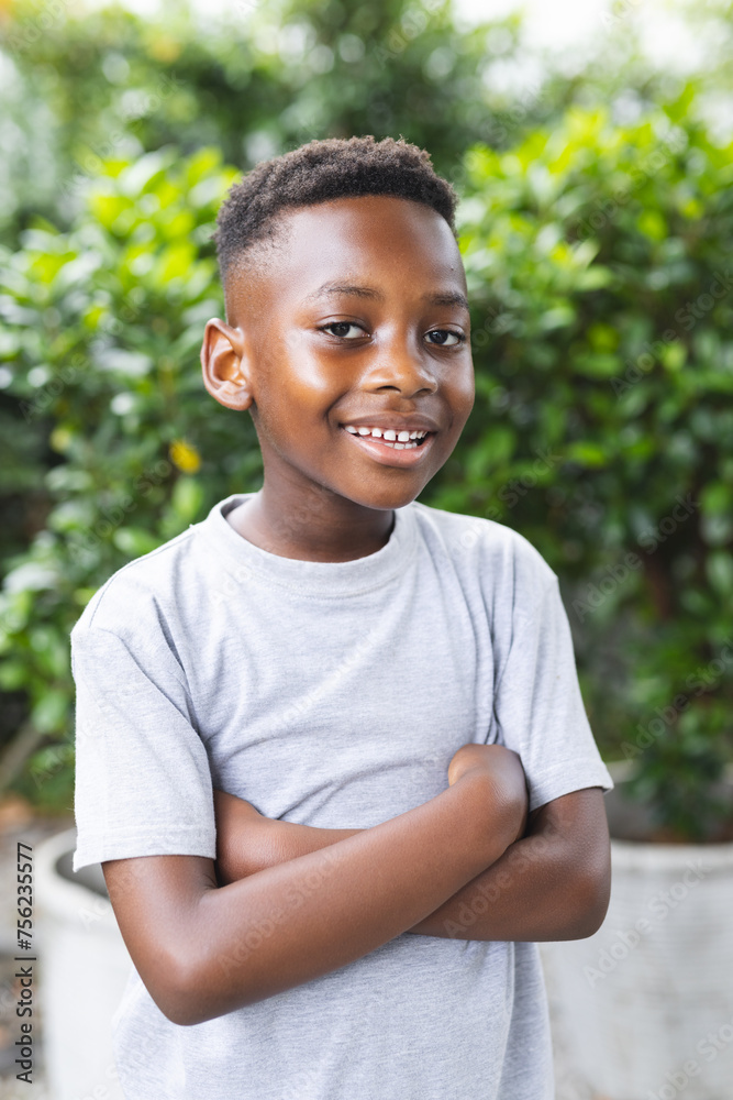 African American boy stands with arms crossed, smiling in an outdoor setting in a garden African American boy stands with arms crossed, smiling in an outdoor setting in a garden