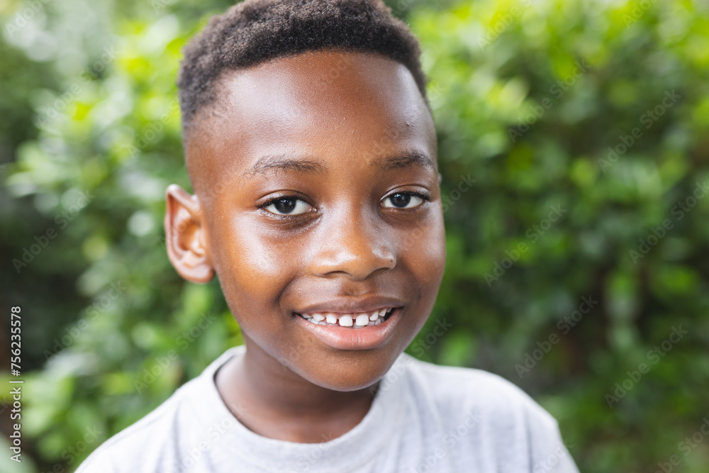 African American boy smiles brightly, surrounded by lush greenery in a garden African American boy smiles brightly, surrounded by lush greenery in a garden