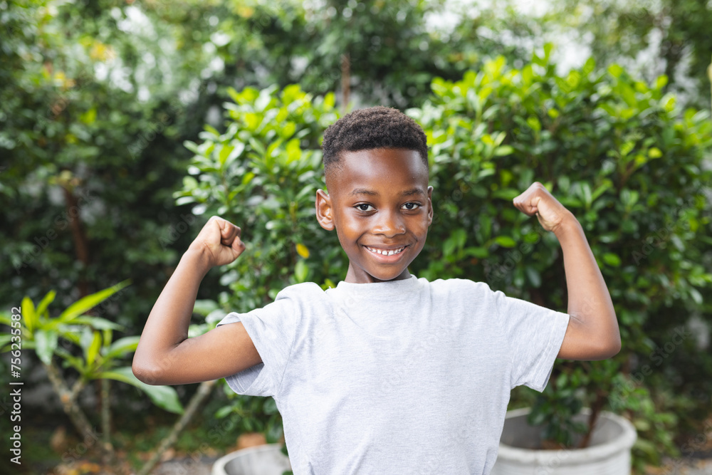 African American boy flexes his muscles with a confident smile in a garden African American boy flexes his muscles with a confident smile in a garden