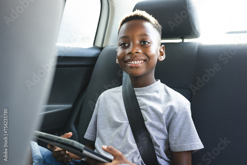 African American boy with a tablet smiles while seated in a car