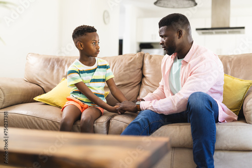 African American father and son sit on a sofa, holding hands and engaging in a serious conversation photo