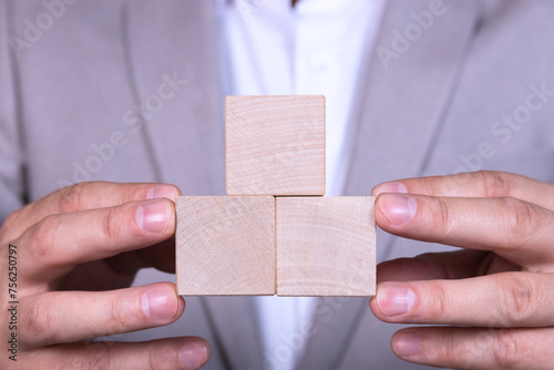 In the Hands of a businessman placing three empty wooden cubes in the shape of a pyramid. Copy space.