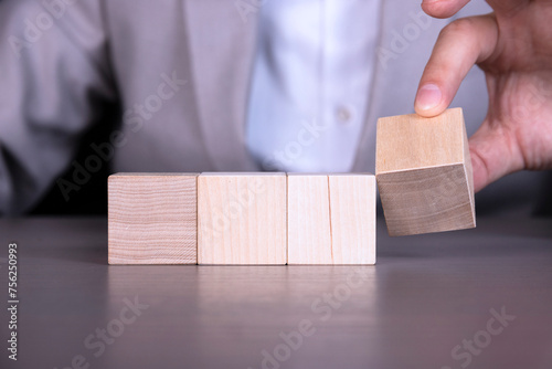 A businessman adds four wooden cubes with empty space for icons, free space for letters, numbers, symbols or labels.