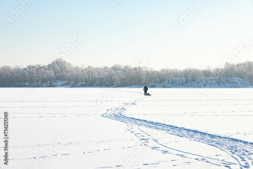 A lonely old hermit, in winter, crosses the river on ice and pulls a sled with firewood for heating photo