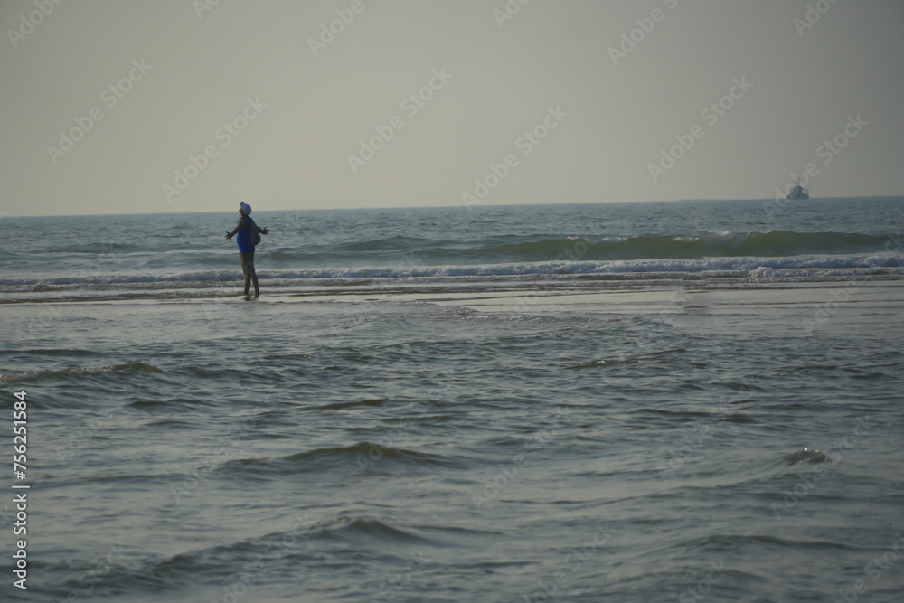 A man walking and enjoying waves of sea. Wavy waters of ocean makes a scenic landscape. Man posing with open arms and enjoying the amazing sunset view at beautiful Arabian sea in Goa, India.