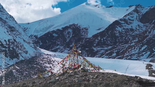 Prayer flags waving in the wind in front of snowy mountain peaks during the sunny day at Shinkula Pass in Himachal Pradesh, India. Snowy mountain peaks of the Shinkula Top during summer season. photo