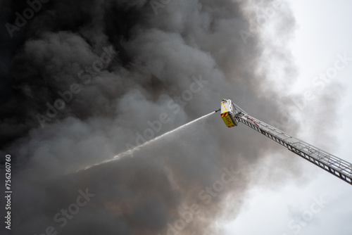 Firefighters in aerial ladder trucks extinguish a fire of industrial hall storing plastic