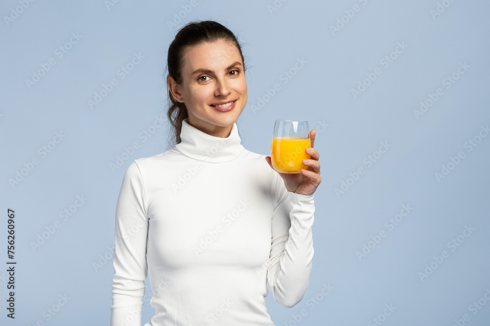 Beautiful young woman drinking a glass of orange juice, healthy lifestyle, on light grey studio background Beautiful young woman drinking a glass of orange juice, healthy lifestyle, on light grey studio background