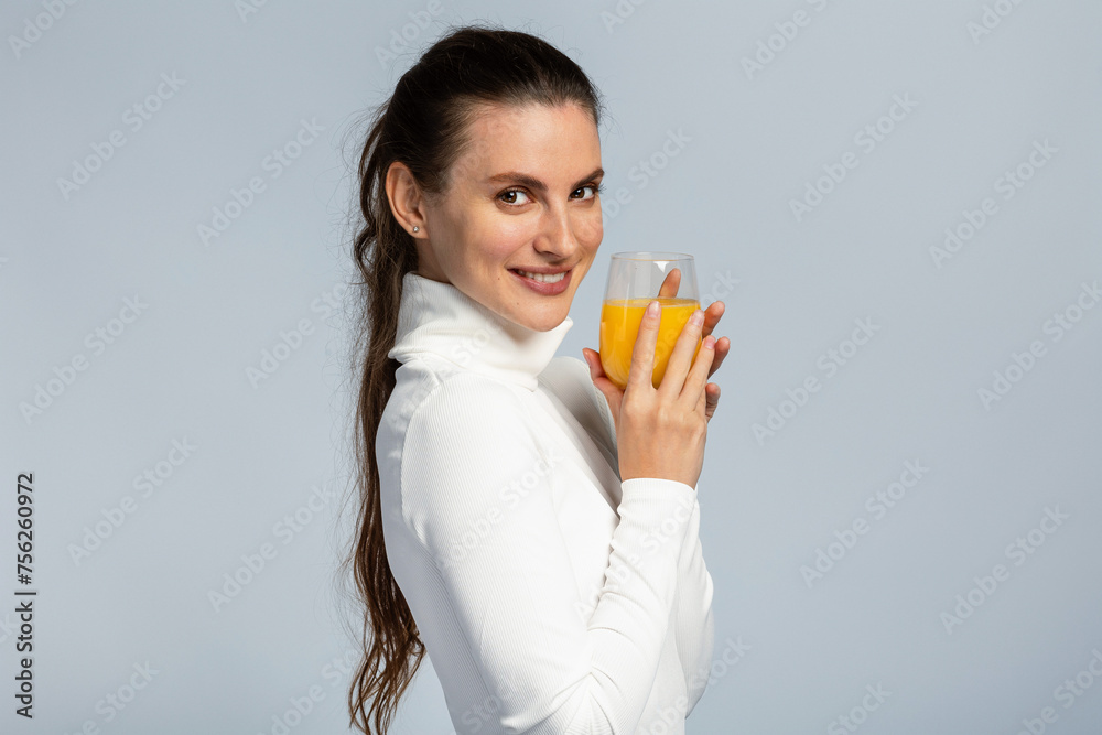 Beautiful young woman drinking a glass of orange juice, healthy lifestyle, on light grey studio background Beautiful young woman drinking a glass of orange juice, healthy lifestyle, on light grey studio background