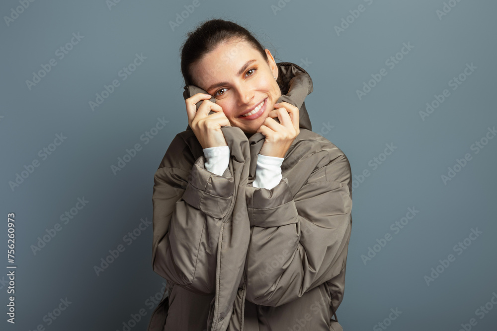 Young cheerful attractive woman wearing a grey coat during autumn and winter, isolated on grey studio background Young cheerful attractive woman wearing a grey coat during autumn and winter, isolated on grey studio background