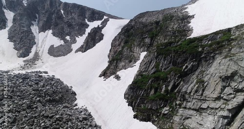 Aerial of snow covered peak, close to cliff to show small waterfalls and small ice cave.