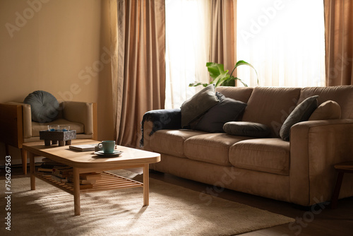 Interior design with beige sofa and wooden coffee table, gray cushions, morning light with sun rays © JpegPhotographer