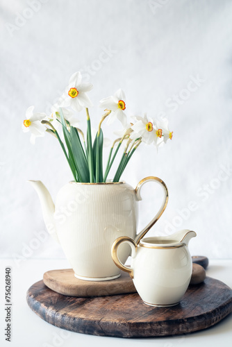 Still life with a blooming bouquet of white daffodils in an elegant porcelain teapot on a textured white background © Jess_Ivanova