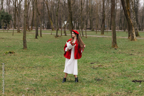 Young woman 20s in red french beret and jacket dressed white dress, walking in city park with bouquet bunch of fresh spring tulips flowers, celebrating International Women's Day, holiday, festive