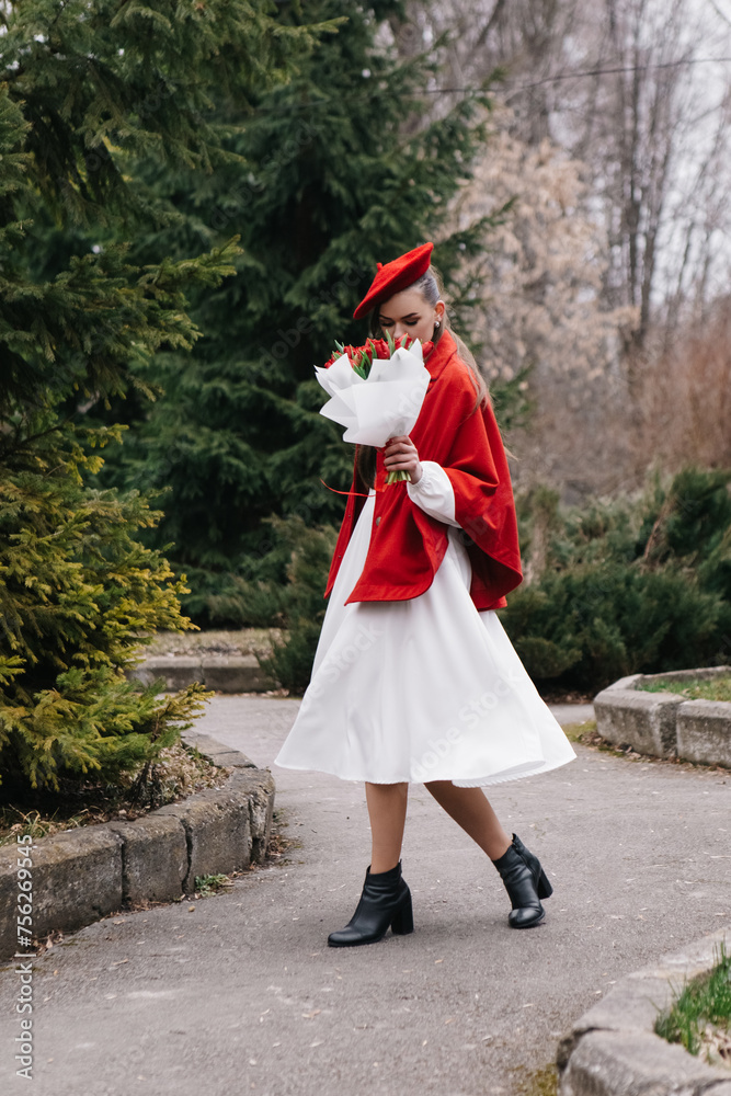 Vertical photo young woman in red french beret and jacket dressed white dress, walking in city park with bouquet bunch of fresh spring tulips flowers, celebrating International Women's Day, holiday
