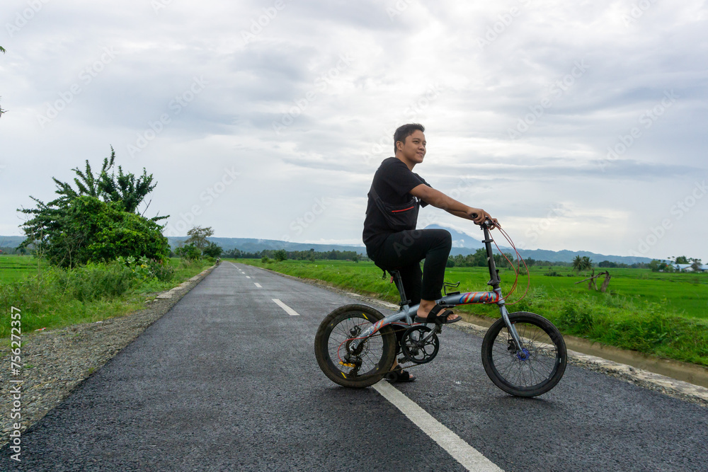 Happy Asian man riding a bicycle at the morning on the asphalt road. Cycling with mountain and paddy rice field view at the background. 