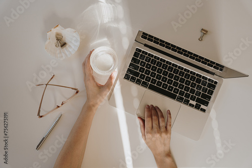 Flatlay of woman working using laptop computer. Comfortable home office workspace. Work at home. Laptop computer, glass of pure water, soft sunlight shadows on table. Flat lay, top view