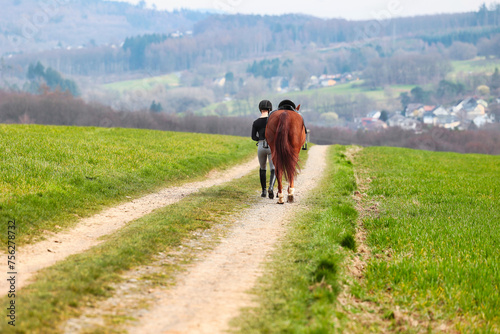 Rider walks her horse along a field path, landscape image in landscape format. © RD-Fotografie
