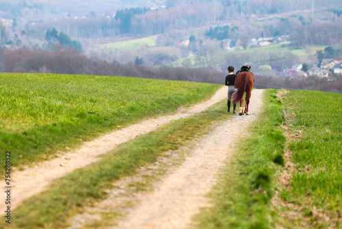 Rider walks her horse along a field path, landscape image in landscape format. © RD-Fotografie