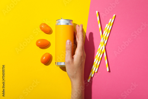Tin can, kumquats, straws and hand on yellow and pink background, top view