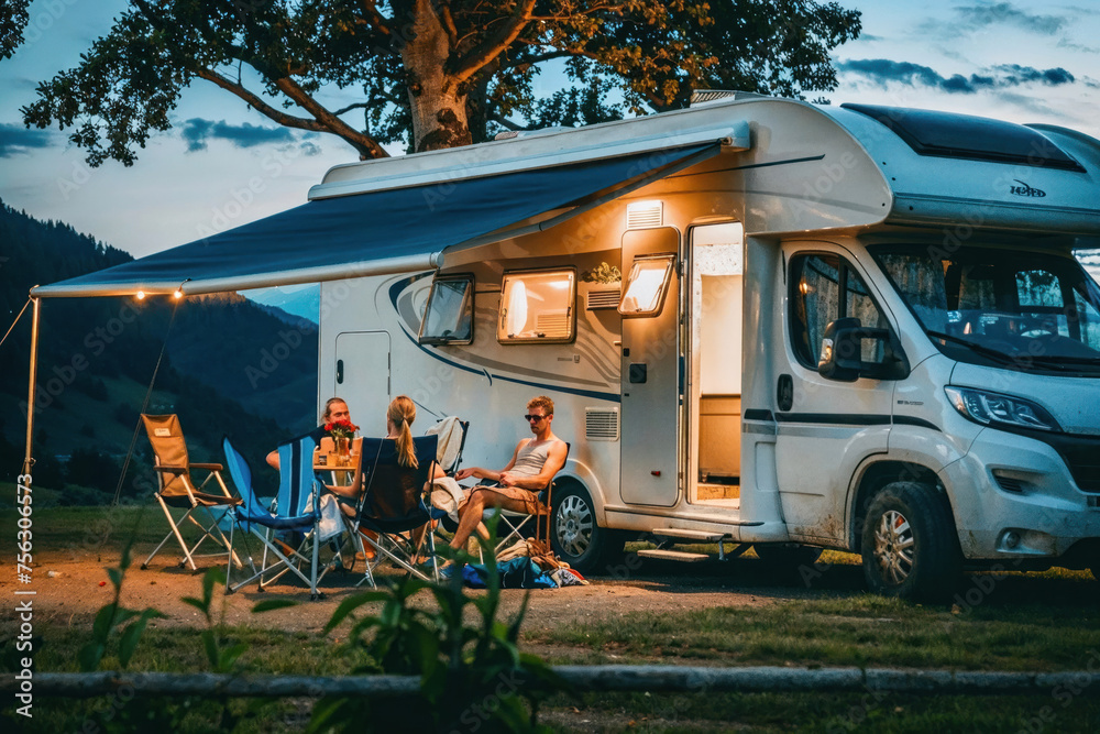 A family spends quality time together outside their RV at a campsite during a calm evening under the twilight sky - obrazy, fototapety, plakaty 