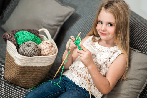 Cute blond little girl knitting on sofa at home enjoying leisure