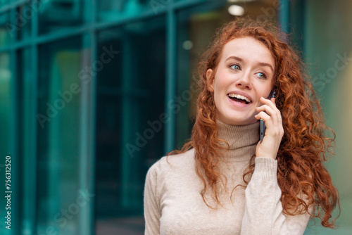 a young redhead enjoying woman in white shirt talking and using on her mobile phone, using mobile in an urban modern city. Lifestyle photos