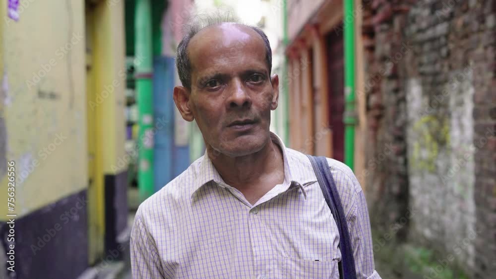 A serious tired partially bald Indian South Asian old or aged male or man carrying an office bag standing in a narrow empty lane and facing or looking at the camera after work hours A serious tired partially bald Indian South Asian old or aged male or man carrying an office bag standing in a narrow empty lane and facing or looking at the camera after work hours