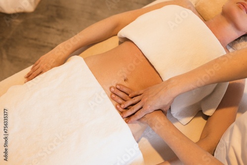 Masseuse is doing belly massage for young woman in massage room of spa salon. Abdominal massage