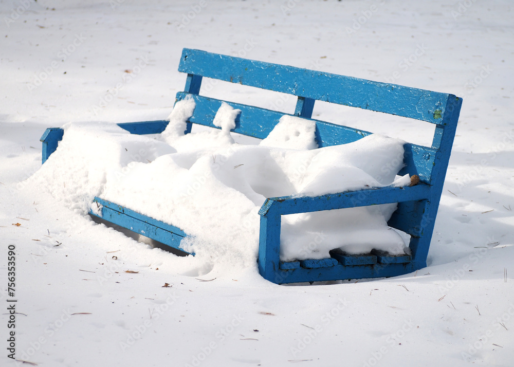Winter background .Blue wooden bench covered with snow in the park.