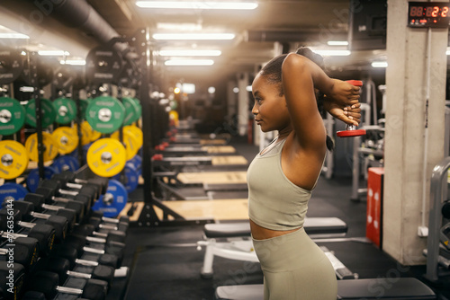 Side view of a fit black sportswoman doing overhead triceps extension with dumbbell at the gym.