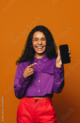 Cheerful woman recommending vibrant fashion on orange background