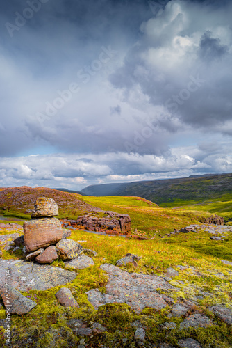 Cover page with Icelandic colorful and wild landscape with lava field covered by ancient moss with stacked stones as a cairns at dramatic rainy sky, Iceland