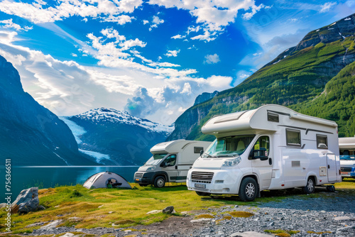 Breathtaking view of motorhomes lined by a tranquil lake with snow-capped mountains under a blue sky