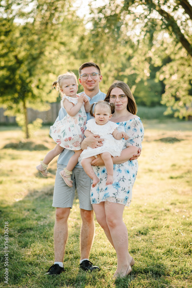 Children hugging parents in nature at sunset. Mom, dad and childs girl walking in the green grass. Happy young family in park spending time together, on vacation, outdoors. Concept of family holiday. Children hugging parents in nature at sunset. Mom, dad and childs girl walking in the green grass. Happy young family in park spending time together, on vacation, outdoors. Concept of family holiday.