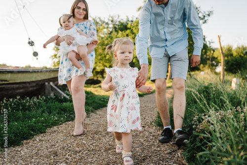 Mom, dad, and kids walking in park at sunset. Mother, father hold hands happy children daughter. Running in green grass in nature on summer day. Concept of family spending time together on a picnic. photo