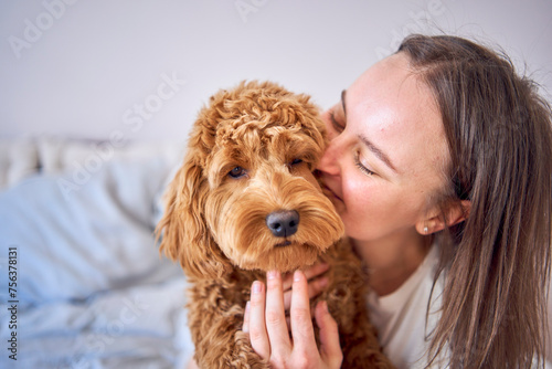 young woman playing and kissing cockapoo girl on bed, minimalism photo