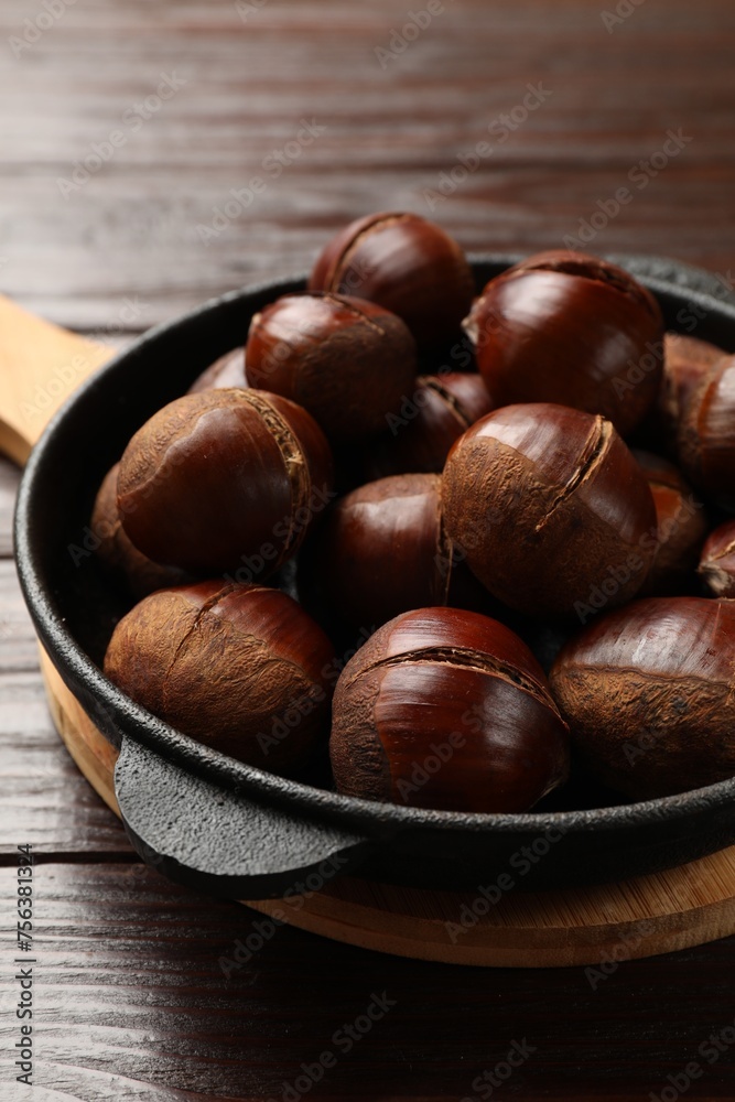 Roasted edible sweet chestnuts in baking dish on wooden table, closeup Roasted edible sweet chestnuts in baking dish on wooden table, closeup