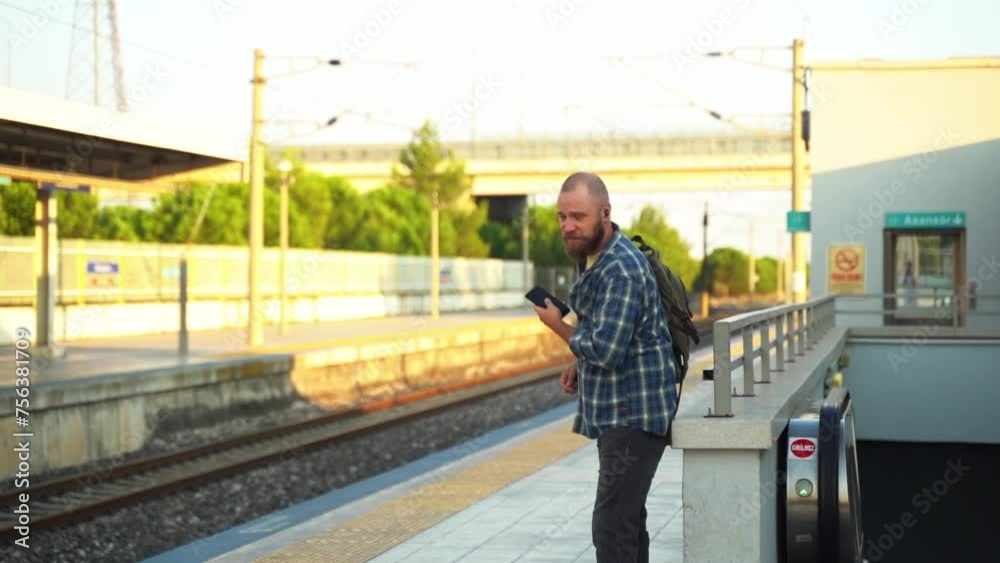 City dweller with a backpack waiting metro train on the platform. An adult heading to work, using a cellphone on public transport. Urban life in the morning as a citizen relies on the subway City dweller with a backpack waiting metro train on the platform. An adult heading to work, using a cellphone on public transport. Urban life in the morning as a citizen relies on the subway