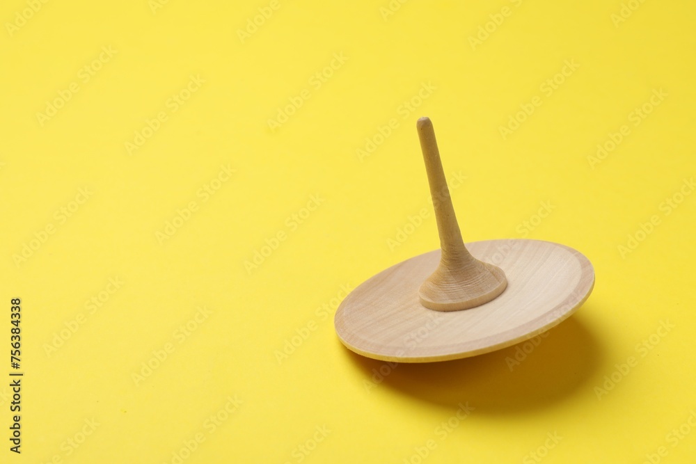 One wooden spinning top on yellow background, space for text One wooden spinning top on yellow background, space for text