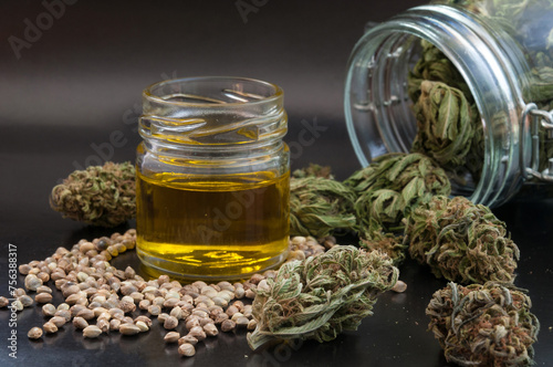 noir still life of hemp products consist of dry flowers of medical marijuana, glass jar with buds, cannabis seeds and small bottle with CBD infused oil close up on black background