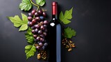 Close-up of a bottle of red wine with a bunch of ripe grapes and green leaves on a dark background