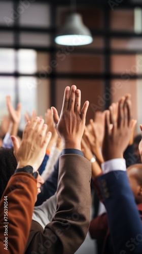 A group of people of various ethnicities are raising their hands in a meeting or classroom.