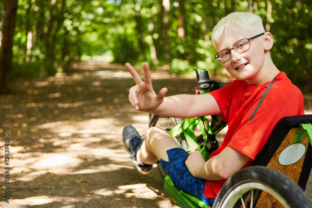 Obraz premium Boy showing peace sign sitting on recumbent bike