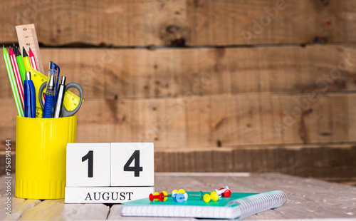 August calendar background with number  14. Stationery pens and pencils in a case on a wooden vintage background. Copy space notepad with pencils and calendar. Planner place for text.