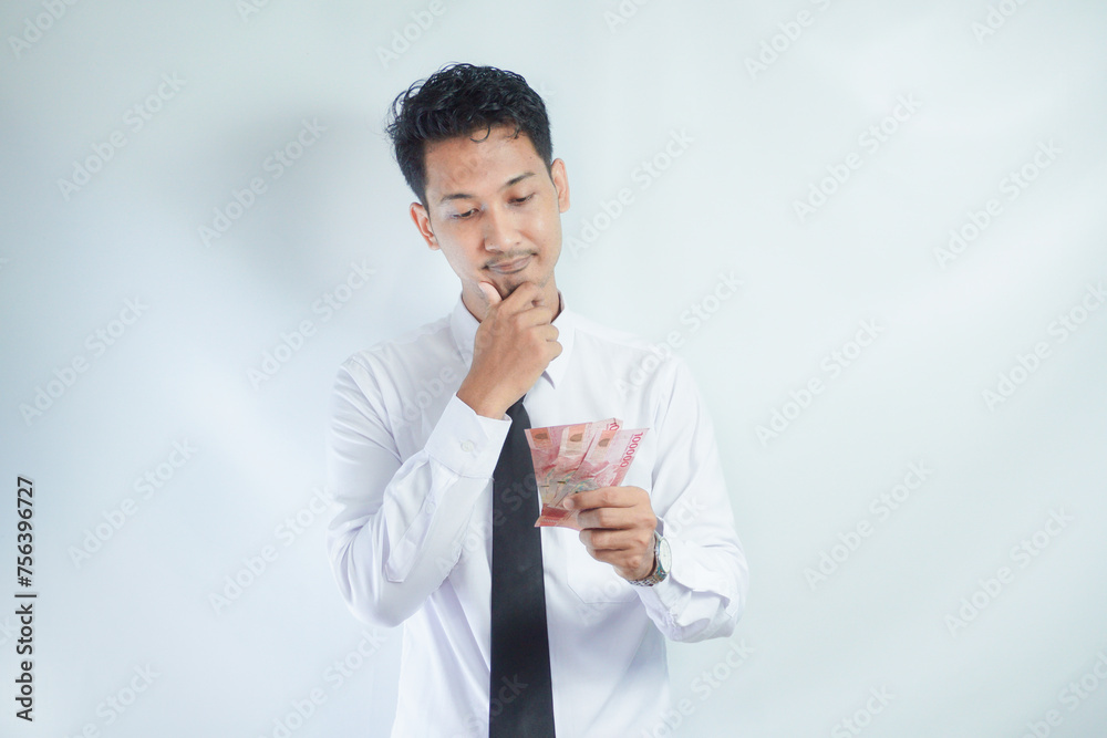 Adult Asian man doing thinking gesture while holding Indonesia paper money Adult Asian man doing thinking gesture while holding Indonesia paper money