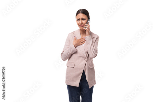 young attractive european brunette woman dressed in a stylish beige jacket is talking on the phone