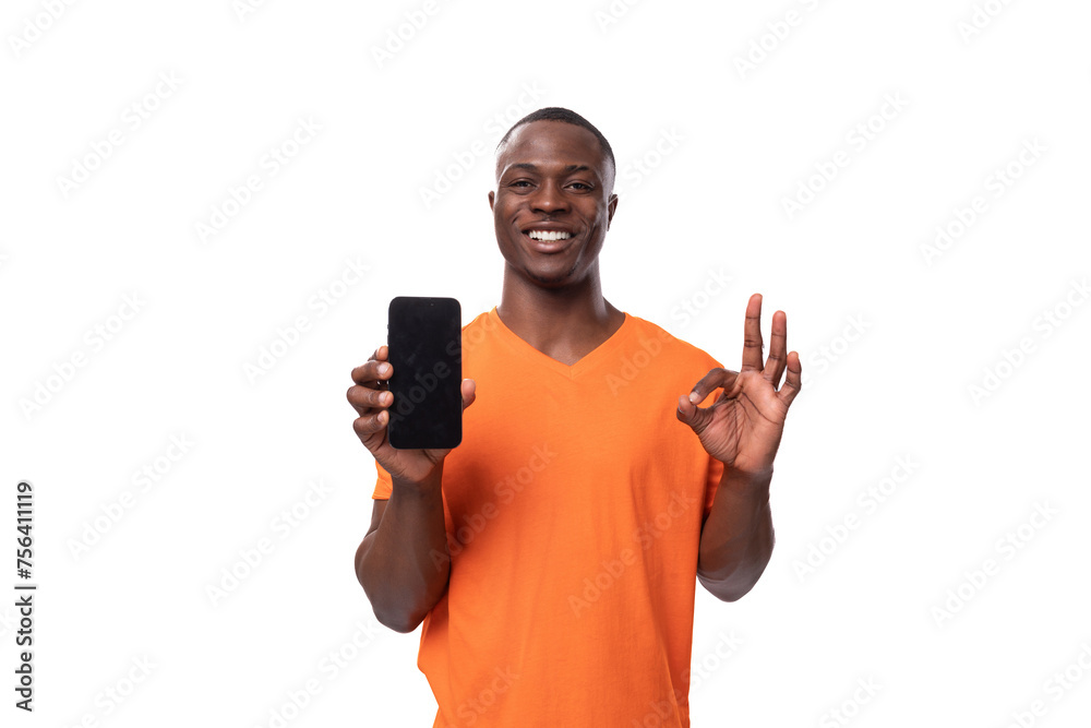young surprised african man dressed in an orange t-shirt holding a phone. advertising concept with mockup young surprised african man dressed in an orange t-shirt holding a phone. advertising concept with mockup